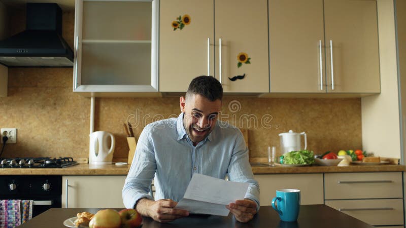 Gut aussehender Mann erhalten Brief der guten Nachrichten Lesein der Küche, während frühen Morgen des Frühstücks zu Hause haben S lizenzfreies stockfoto Gut aussehender Mann erhalten Brief der guten Nachrichten Lesein der Küche, während frühen Morgen des Frühstücks zu Hause haben S lizenzfreies stockfoto
