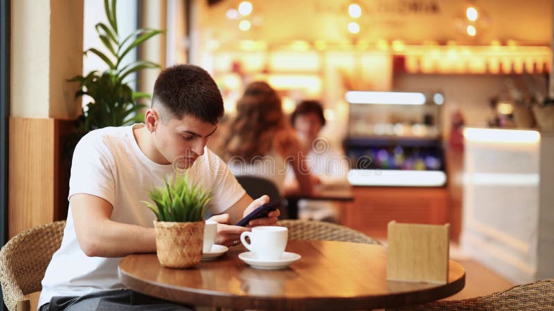 Guy in cafe drinks coffee and calling using mobile phone stock video footage