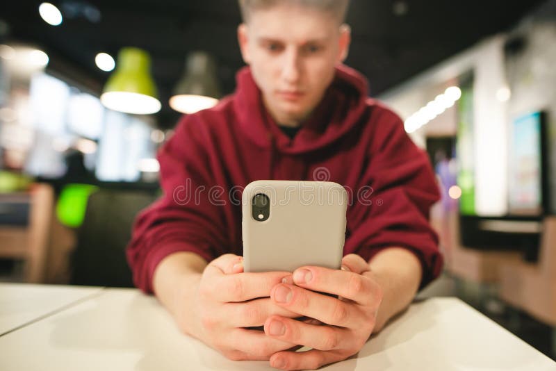 Guy in casual clothing uses a smartphone in a fast food cafe, focusing on a modern smartphone in the hands of a man stock photo Guy in casual clothing uses a smartphone in a fast food cafe, focusing on a modern smartphone in the hands of a man stock photo
