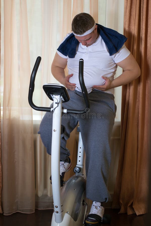 Guy Exercising on Stationary Training Bicycle and Looking at His Fat