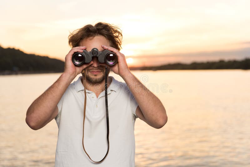 Curly guy with binoculars looking for something during sunset royalty free stock images