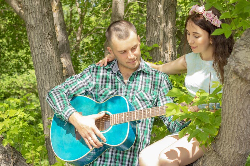 The guy plays guitar to his girlfriend. romantic meeting. girl sitting in a tree royalty free stock photo The guy plays guitar to his girlfriend. romantic meeting. girl sitting in a tree royalty free stock photo
