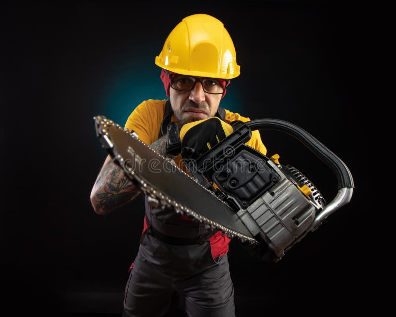A Guy in Protective Overalls with a Chainsaw on a Dark Background Stock