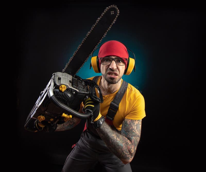 A Guy in Protective Overalls with a Chainsaw on a Dark Background Stock