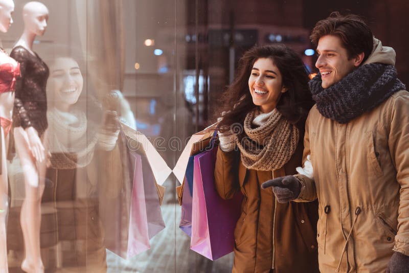 Guy som pekar på Shopwindow och går med flickvän i natts stad royaltyfria foton Guy som pekar på Shopwindow och går med flickvän i natts stad royaltyfria foton