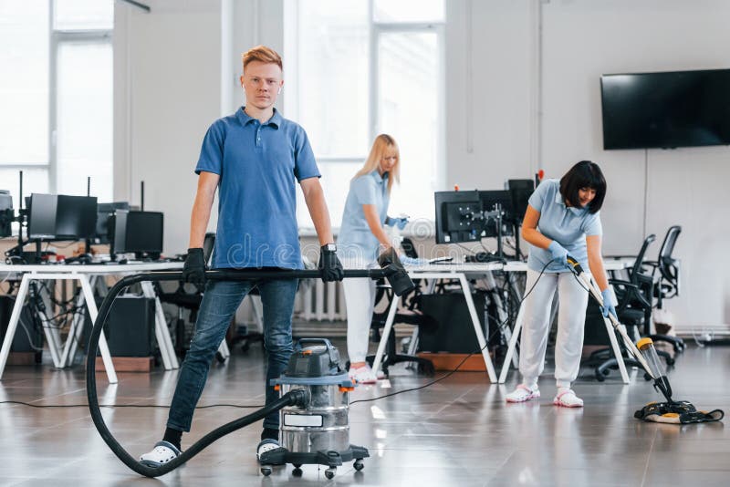 Guy with Vacuum Cleaner. Group of Workers Clean Modern Office Together