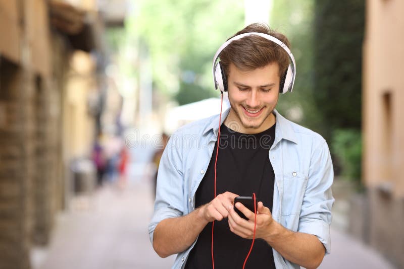 Happy guy walking and using a smart phone to listen music with headphones. Happy guy walking and using a smart phone to listen music with headphones