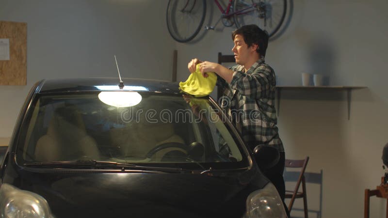 A guy washes the roof of his car with a rag. A guy washes the roof of his car with a rag