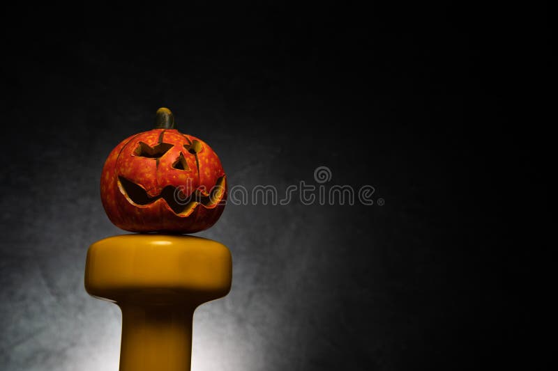 Gym Halloween composition with decorative pumpkin on a dumbbell and copy space.