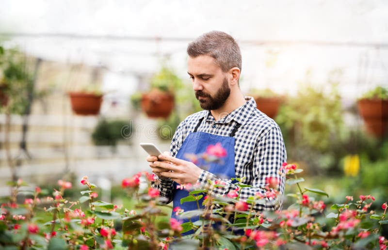 Gardener, business owner making phone call with customer or supplier, standing in front flowers and seedlings. Small greenhouse business. Gardener, business owner making phone call with customer or supplier, standing in front flowers and seedlings. Small greenhouse business.