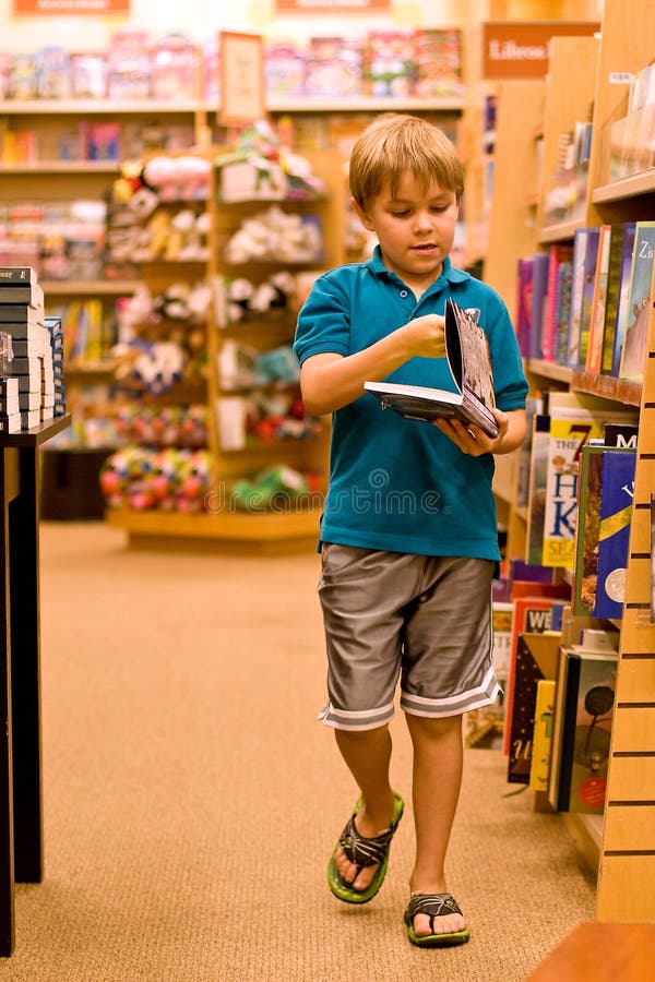 A seven year old boy walks in the libary, holding a book in his hands. He wears a turquoise blue polo shirt and shorts and turns the pages in a book. A seven year old boy walks in the libary, holding a book in his hands. He wears a turquoise blue polo shirt and shorts and turns the pages in a book.