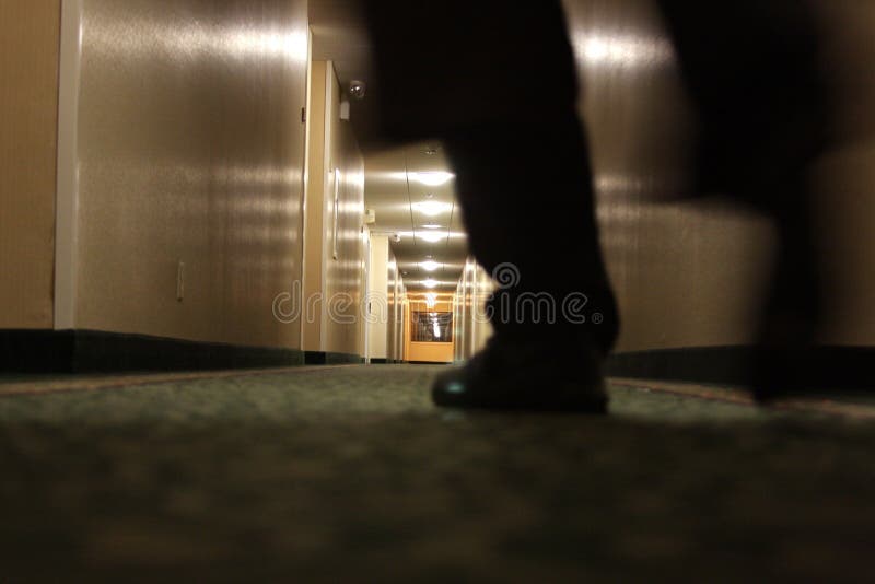 A dark, floor-level view of a man's feet as he walks down a dimly lit hotel hallway. Some motion blur. A dark, floor-level view of a man's feet as he walks down a dimly lit hotel hallway. Some motion blur.