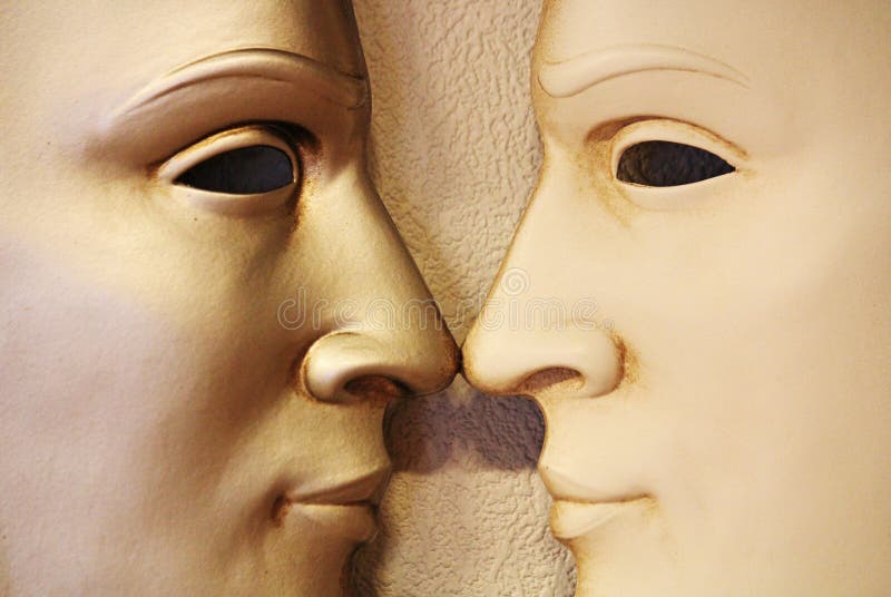 A close up view of an Italian Venetian mask showing two identical faces, nose to nose with a very blank, cold expression on their faces showing no emotion. A close up view of an Italian Venetian mask showing two identical faces, nose to nose with a very blank, cold expression on their faces showing no emotion.
