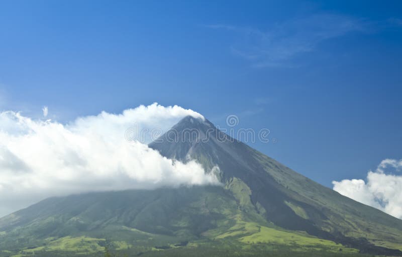Mt mayon volcano smoking against a blue sky, with dark trail of lava marking the sides from a recent eruption. Mt mayon volcano smoking against a blue sky, with dark trail of lava marking the sides from a recent eruption