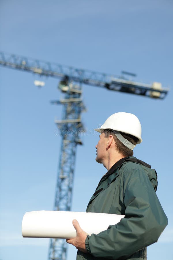 Constructor in hardhat with blueprints against modern crane. Constructor in hardhat with blueprints against modern crane