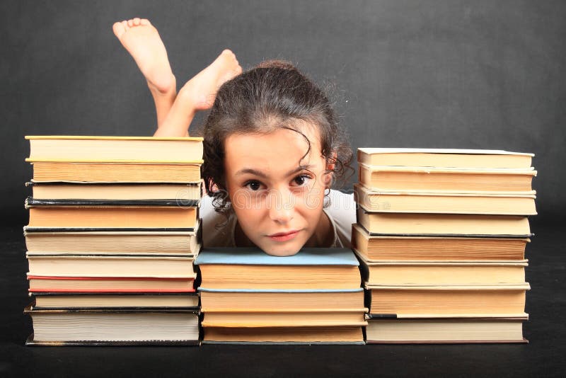 Sad or angry teenage girl - head of kid lying on old books between two others stacks of old books with soles of her bare feet behind on black background. Entertainment and education concept. Sad or angry teenage girl - head of kid lying on old books between two others stacks of old books with soles of her bare feet behind on black background. Entertainment and education concept.