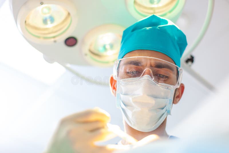Beautiful portrait of a surgeon doctor at work. The lamp in the background. The surgeon gives injections to the head. Baldness treatment. Hair transplant. Surgeons in the operating room carry out hair transplant surgery. Surgical technique that moves hair follicles from a part of the head.