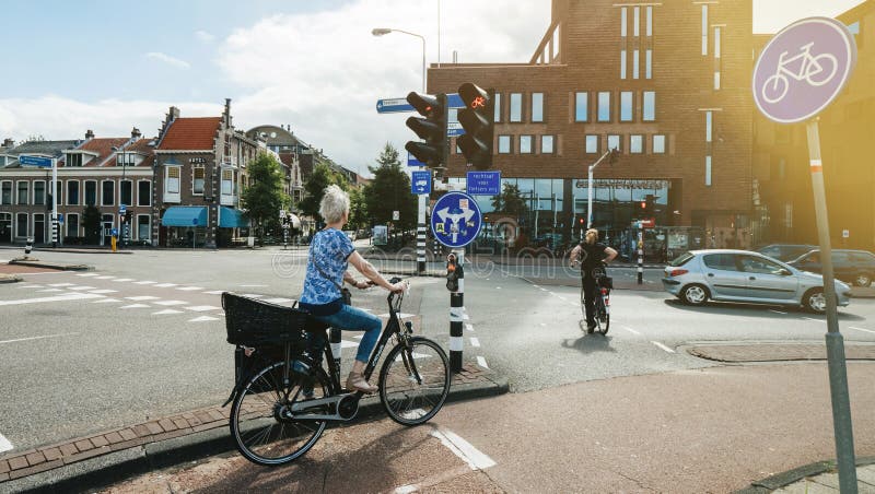 Haarlem, Netherlands - Aug 16, 2018: Side view of elegant Dutch woman waiting for green light riding a city bicycle - bike blue sign. Haarlem, Netherlands - Aug 16, 2018: Side view of elegant Dutch woman waiting for green light riding a city bicycle - bike blue sign