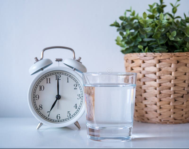 Habitude quotidienne de boire de l'eau chaude tous les matins. un verre d'eau potable avec horloge vintage montrant 7 heures sur l