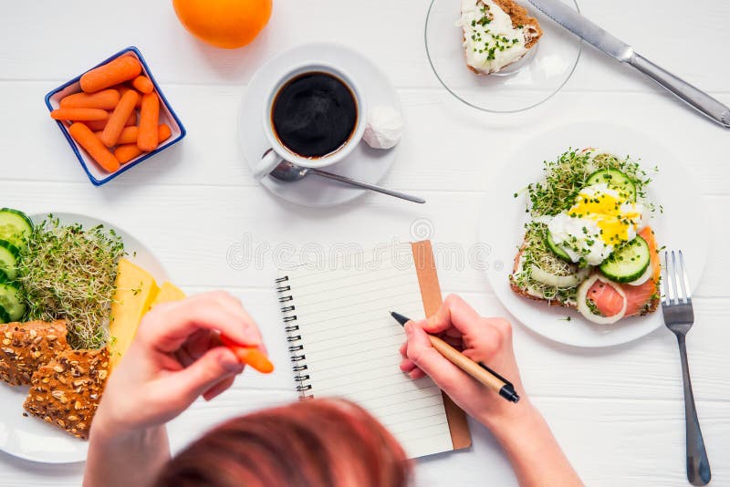 Habitudes de matin des personnes réussies Planification de jour et repas sain Femme mangeant la carotte et écrivant dans le carne photos libres de droits Habitudes de matin des personnes réussies Planification de jour et repas sain Femme mangeant la carotte et écrivant dans le carne photos libres de droits