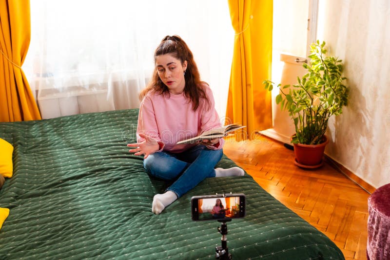 Hablando de una mujer sentada en una cama y vlogueando con un smartphone creando contenido de alta calidad en medios sociales para imagenes de archivo