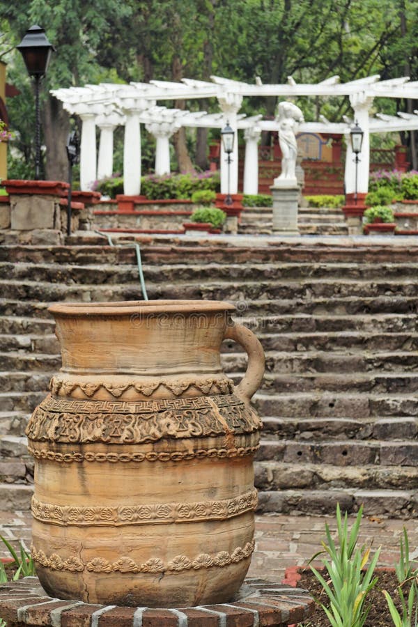 A ceramic vase in the first plane and the gardens of a typical mexican hacienda farm house with an iron street lamp and a naked woman marble sculpture in the back. City of Guanajuato, mexican colonial heartland of mexico. A ceramic vase in the first plane and the gardens of a typical mexican hacienda farm house with an iron street lamp and a naked woman marble sculpture in the back. City of Guanajuato, mexican colonial heartland of mexico.