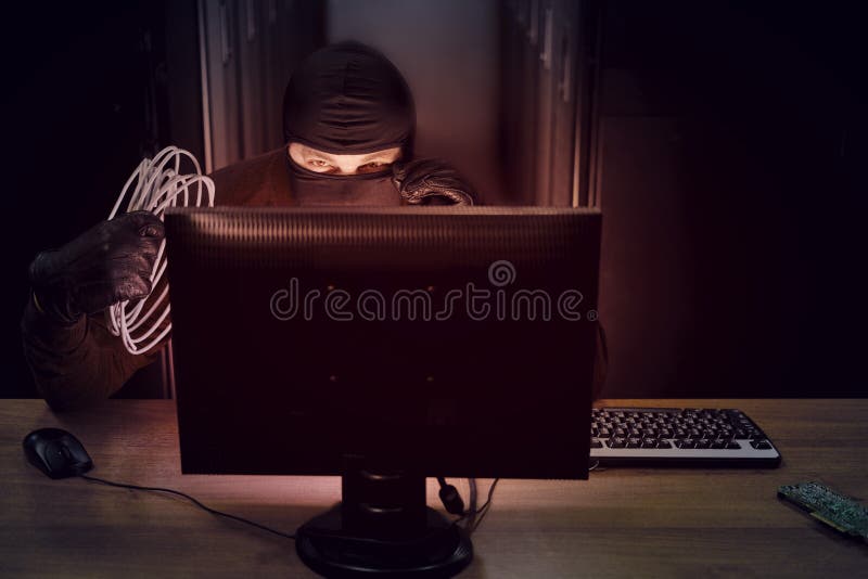 A hacker in a black mask with wires in his hand in a server room. Concept of data security problems and network hacking royalty free stock image