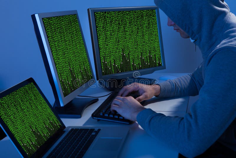 Hacker in hooded jacket using computer at table royalty free stock photo