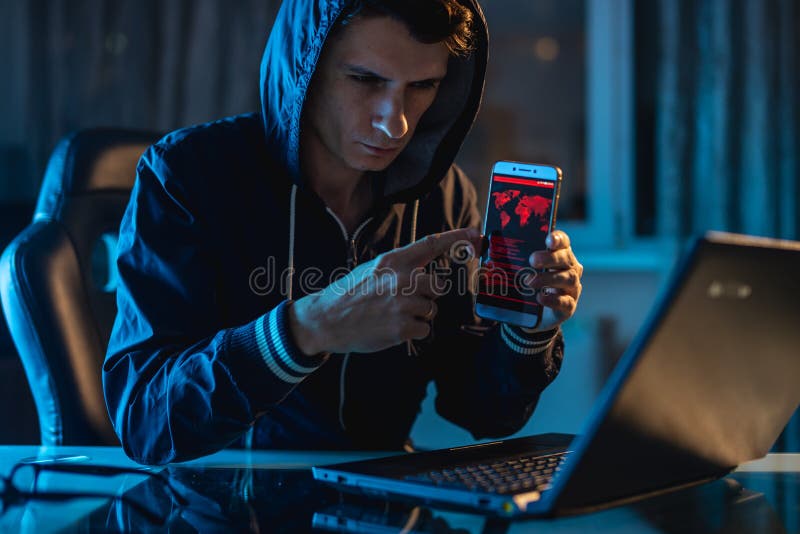 Hacker trzyma telefon w jego w kapiszonie wr?cza pr?bowa? kra?? dojazdowych baza danych z has?ami CyberSecurity obraz royalty free Hacker trzyma telefon w jego w kapiszonie wr?cza pr?bowa? kra?? dojazdowych baza danych z has?ami CyberSecurity obraz royalty free