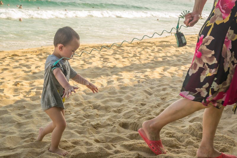 Hainan, Chine - 15 mai 2019 : une femme mène un petit enfant attaché sur une laisse sur la plage photographie stock Hainan, Chine - 15 mai 2019 : une femme mène un petit enfant attaché sur une laisse sur la plage photographie stock