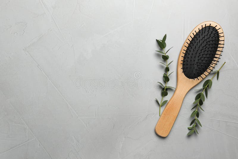 Hair brush and green twigs on grey stone background, flat lay. Space for text
