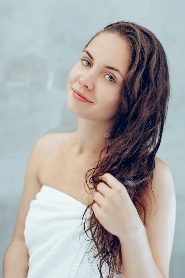 Hair skin care concept. Beautiful young woman touching her wet hair with hands and smiling while standing in front of the mirror stock photos Hair skin care concept. Beautiful young woman touching her wet hair with hands and smiling while standing in front of the mirror stock photos