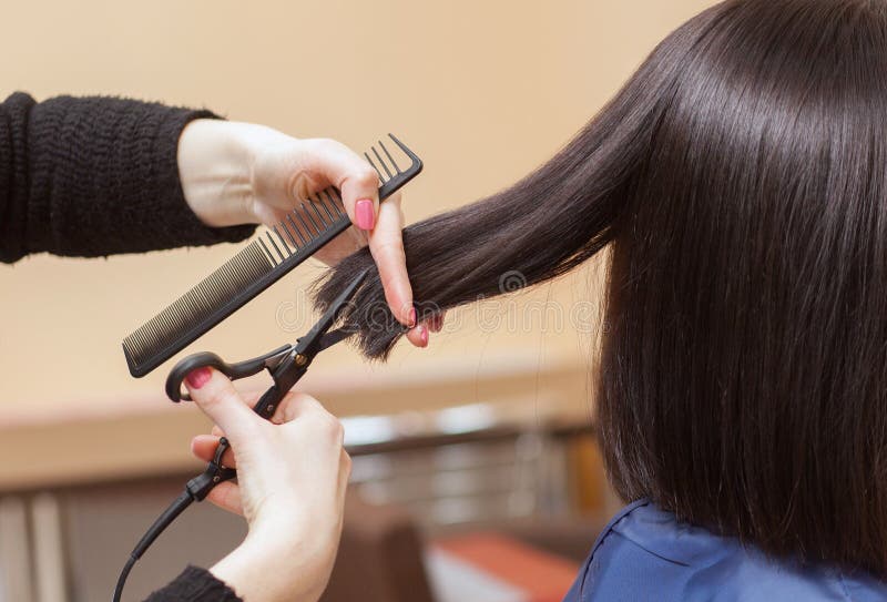 Estilista tiene caliente tijeras de cabello sobre el joven, morena en belleza.