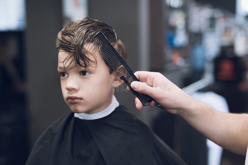 The hairdresser makes a fashionable pretty hairstyle for the boy in a modern barbershop. stock image The hairdresser makes a fashionable pretty hairstyle for the boy in a modern barbershop. stock image