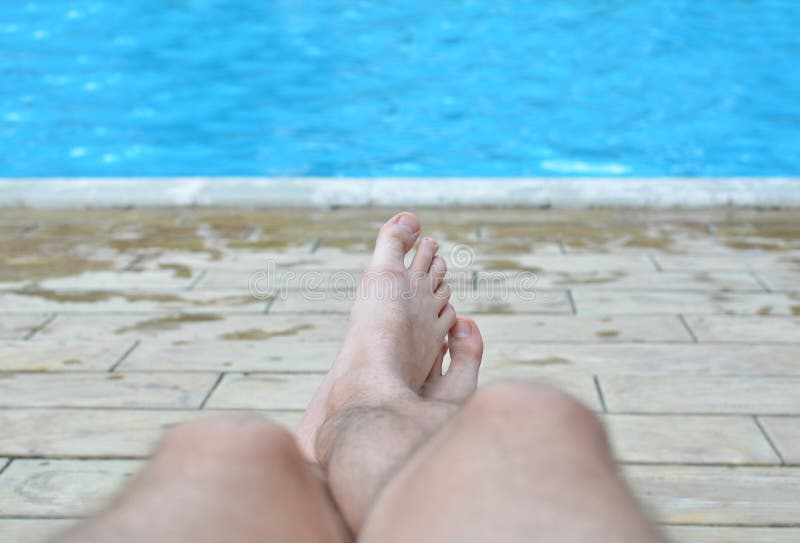 Hairy legs of a man against a background of pure blue water in a pool. A tired man finally relaxed by the water. The concept of the long-awaited holiday. All inclusive. Sunbathe.