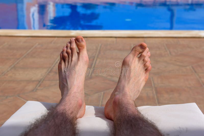 Hairy man`s legs, during taking sunbath. Hot day near outdoors swimming pool.