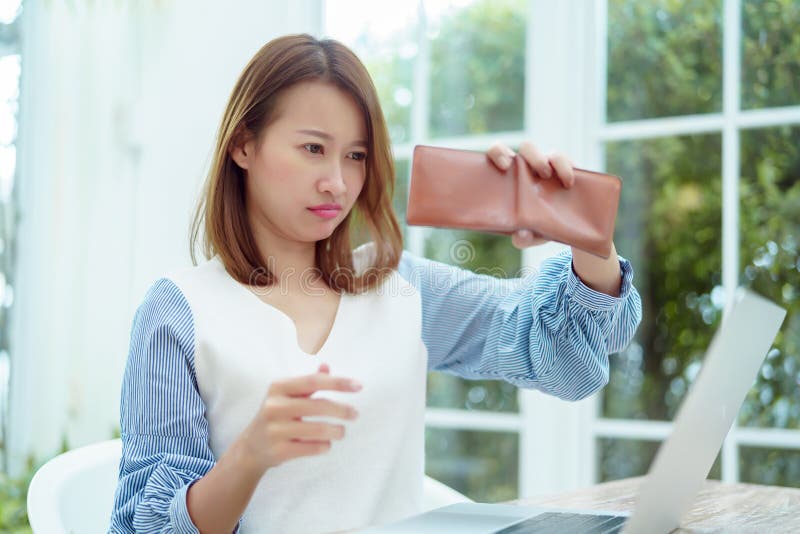 Half-body portrait of an Asian woman in a white shirt sitting in a bakery examining her purse for money with a stressed, unhappy