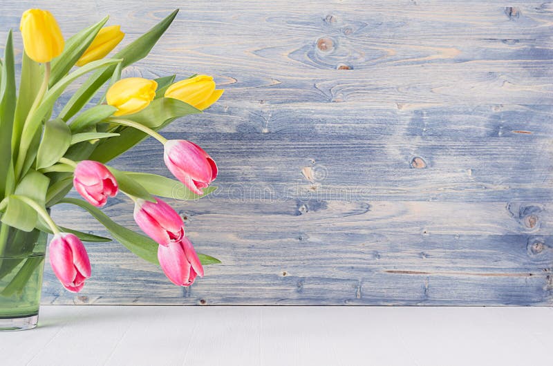 Half bouquet red and yellow tulips in green glass vase on blue shabby wooden background with copy space. Spring easter home decor.