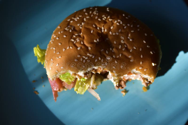 A Halfeaten Meat Burger with Vegetables on a Blue Plate Stock Image