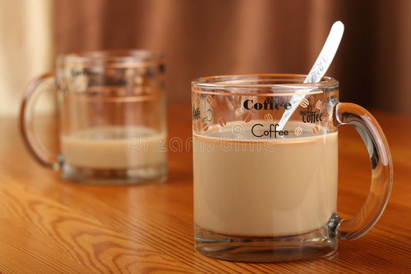 Half-empty and full transparent glass cup with coffee and milk on a wooden table