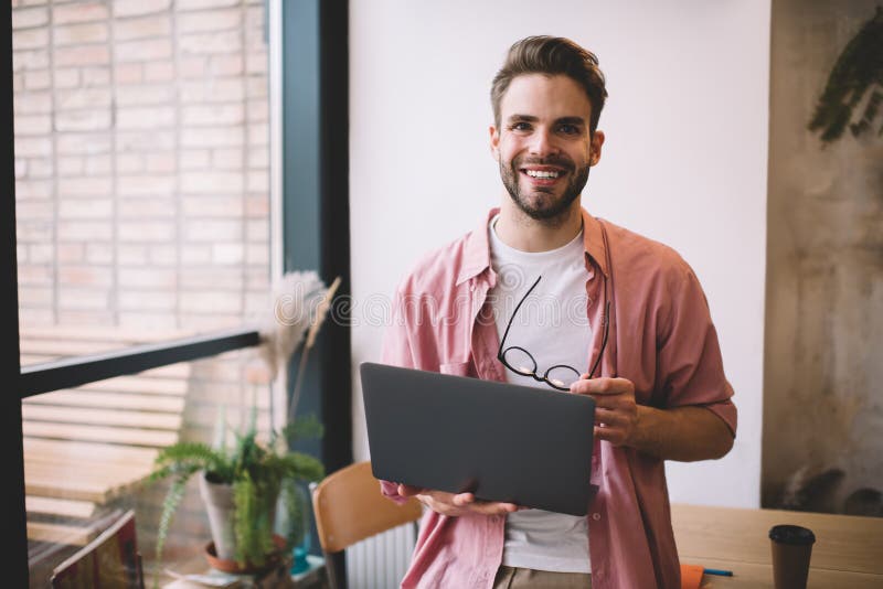 Half length of cheerful male freelancer with laptop device and spectacles in hands smiling at camera during work break, joyful Caucaisan programmer with digital netbook enjoying time for networking. Caucaisan man stock images, royalty-free photos and pictures