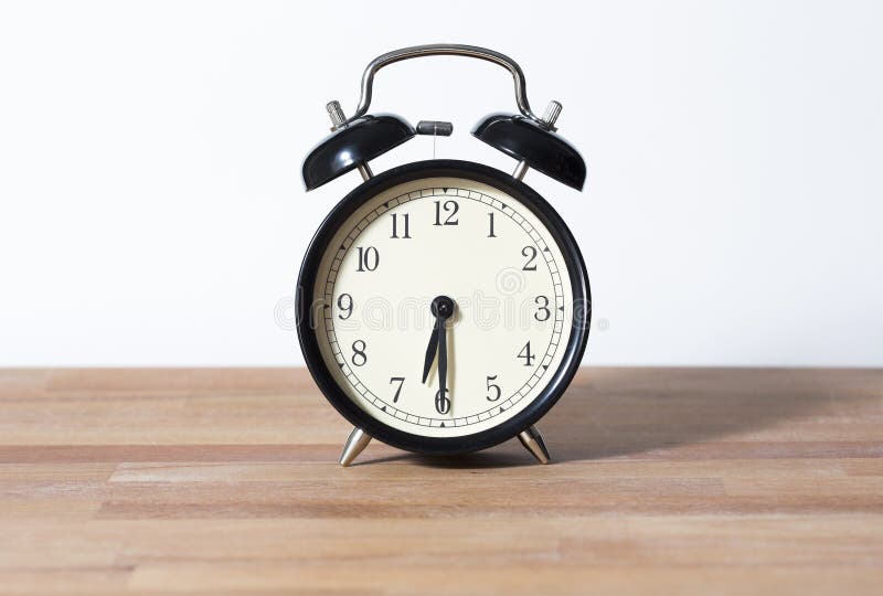 The time is 6:30 am or pm. it is half past six. A retro clock isolated on a wooden table and white background. The time is 6:30 am or pm. it is half past six. A retro clock isolated on a wooden table and white background.