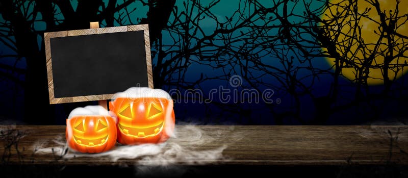 Halloween background.Pumpkin with smoke on grunge blackboard on wood table at spooky dead tree and full moon in blue gradient