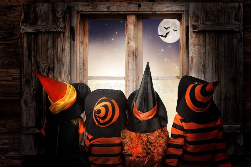 halloween Barn i dräkter av häxor och trollkarlen på natten sitter nära en fönsterandandblick på himlen och slagträna arkivfoton halloween Barn i dräkter av häxor och trollkarlen på natten sitter nära en fönsterandandblick på himlen och slagträna arkivfoton
