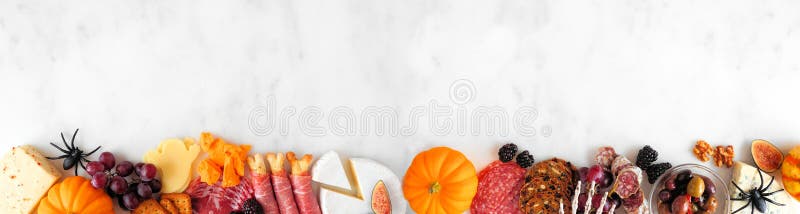 Halloween charcuterie border against a white marble banner background. Selection of cheese and meat appetizers. Copy space