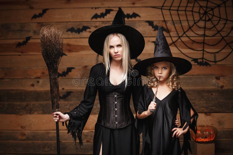 Halloween Concept - cheerful mother and her daughter in witch costumes celebrating Halloween posing with curved pumpkins over bats