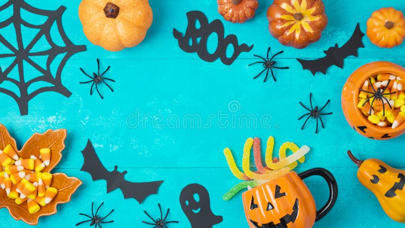 Halloween holiday background with jack o lantern pumpkin, candy corn and decorations on blue wooden board. View from above. Flat lay