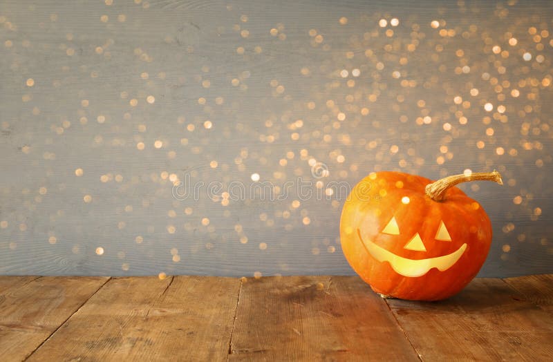 Halloween holiday concept. Cute pumpkin on wooden table and glitter lights overlay