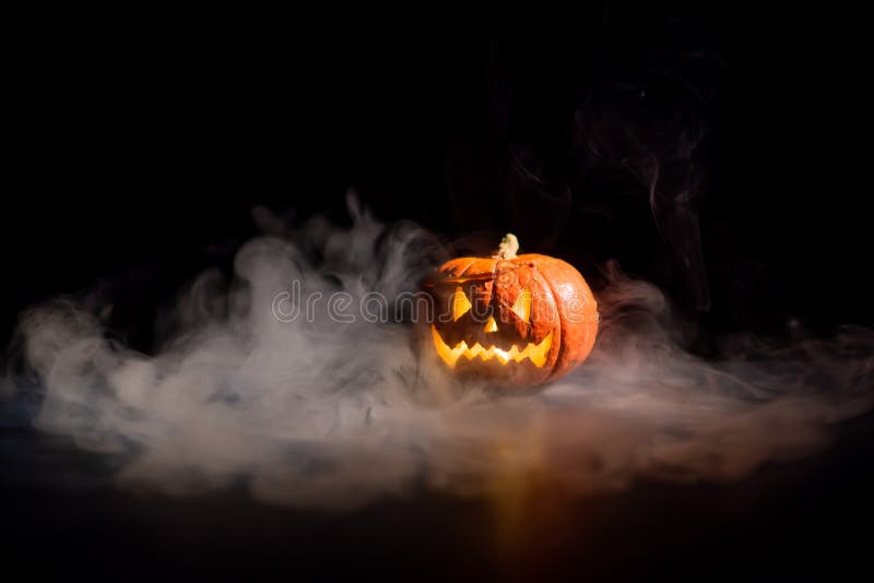 Halloween, orange pumpkin with a scary luminous face on a dark background. Gray thick smoke comes out. stock photos Halloween, orange pumpkin with a scary luminous face on a dark background. Gray thick smoke comes out. stock photos