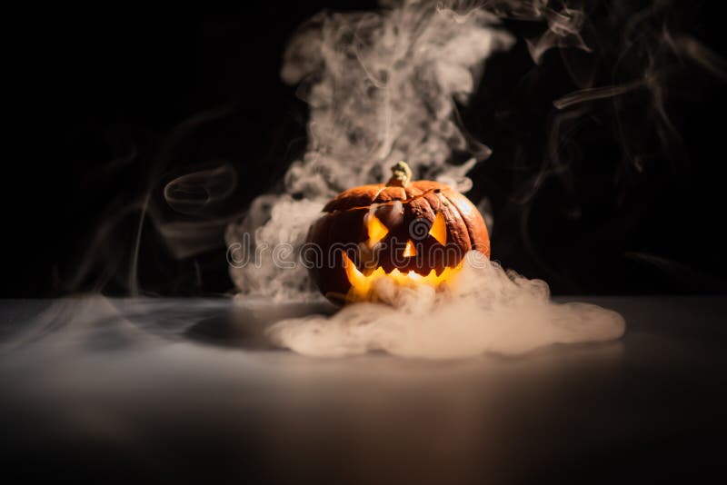 Halloween, orange pumpkin with a scary luminous face on a dark background. Gray thick smoke comes out royalty free stock photo Halloween, orange pumpkin with a scary luminous face on a dark background. Gray thick smoke comes out royalty free stock photo